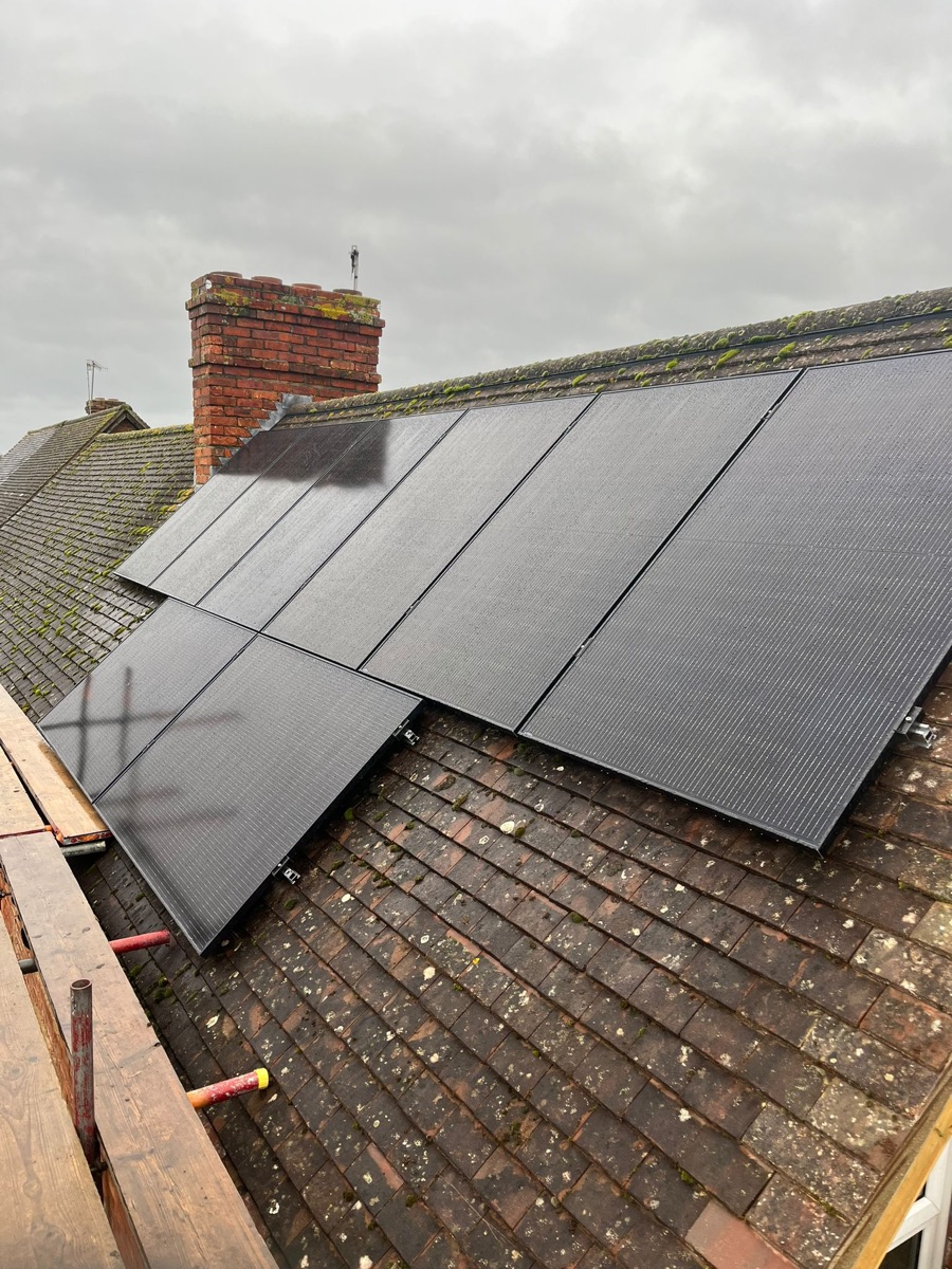 Black solar panels on an old clay-tiled roof beside a brick chimney